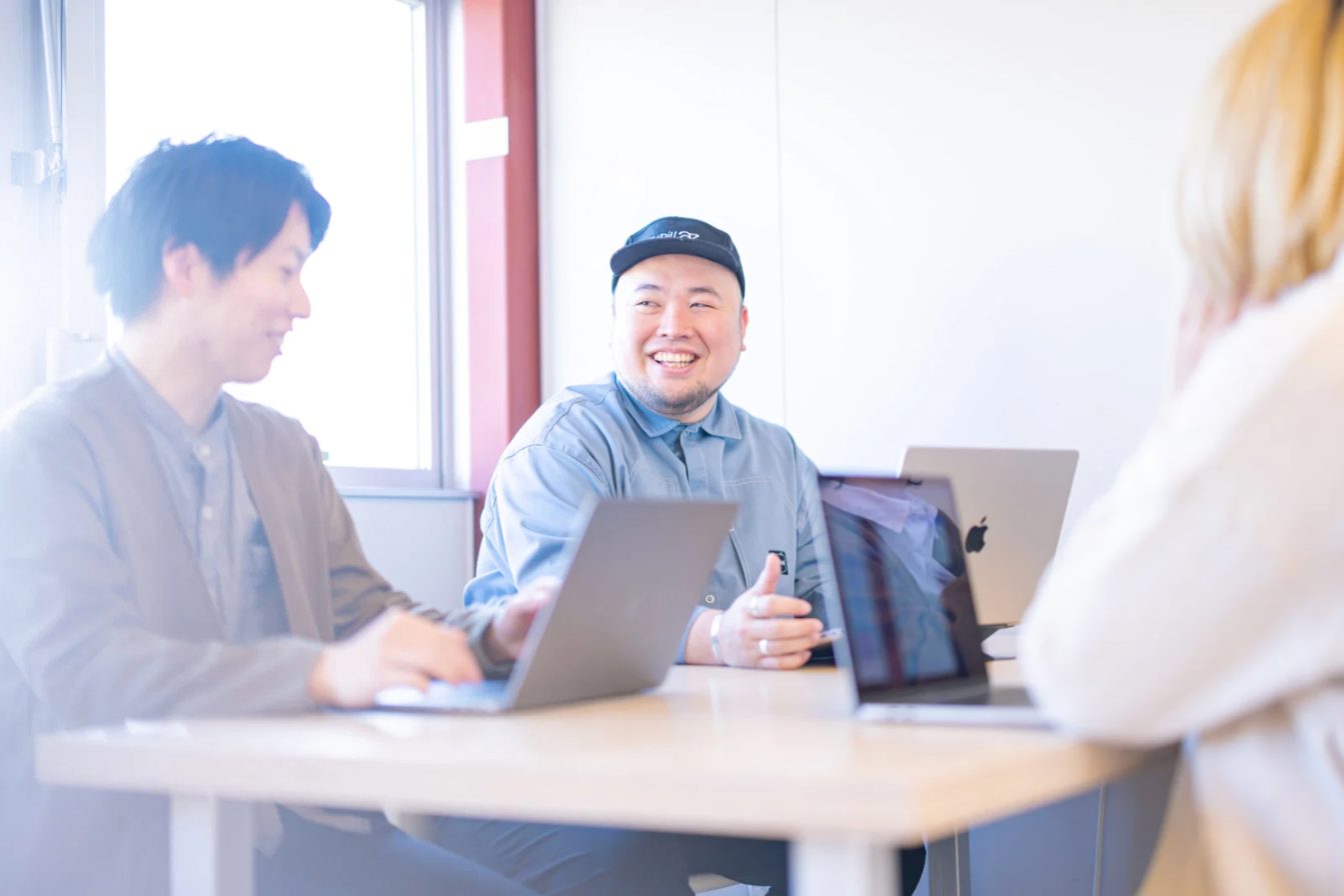 ノートパソコンを囲んで楽しそうに話す人たち（イメージ）